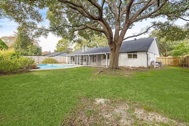 back of house featuring a sunroom, a fenced in pool, and a lawn