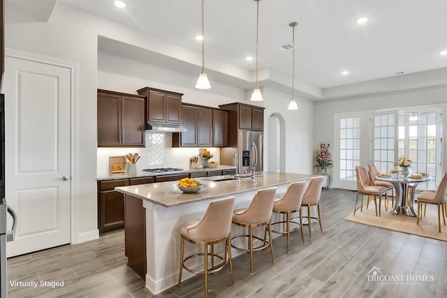 kitchen with a kitchen breakfast bar, light stone counters, stainless steel appliances, pendant lighting, and an island with sink