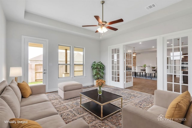 living room featuring a tray ceiling, ceiling fan, french doors, and light hardwood / wood-style floors