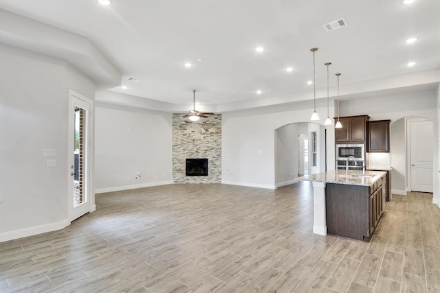 kitchen with light stone countertops, a kitchen island with sink, sink, decorative light fixtures, and stainless steel microwave