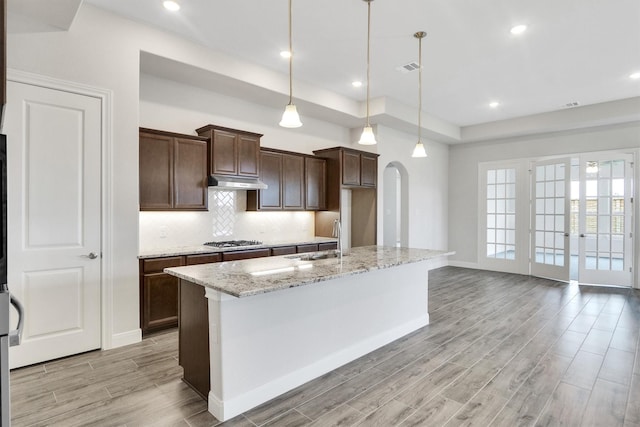 kitchen featuring sink, hanging light fixtures, light stone counters, an island with sink, and stainless steel gas stovetop