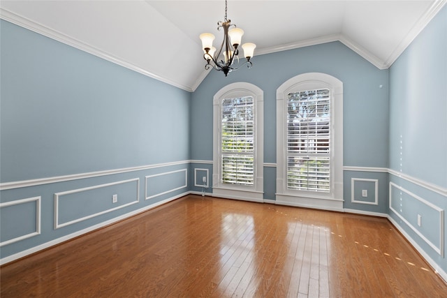 empty room featuring lofted ceiling, wood-type flooring, ornamental molding, and an inviting chandelier