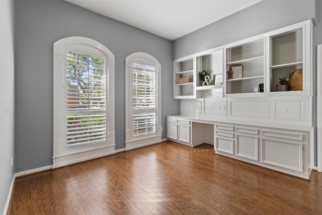 unfurnished office featuring dark hardwood / wood-style flooring and built in desk