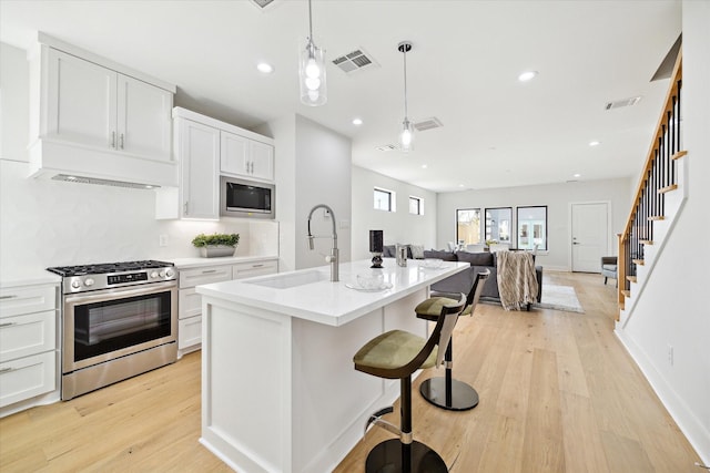 kitchen featuring sink, stainless steel appliances, an island with sink, decorative light fixtures, and white cabinets