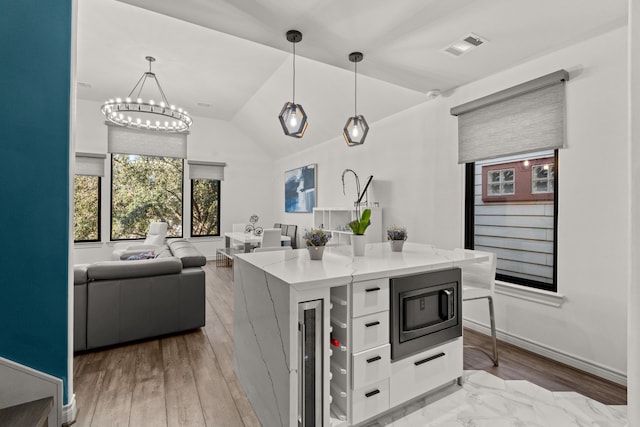 kitchen with white cabinetry, hanging light fixtures, light stone counters, built in microwave, and vaulted ceiling