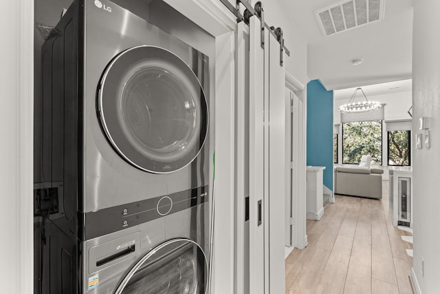 laundry area featuring light hardwood / wood-style flooring, a barn door, and stacked washing maching and dryer