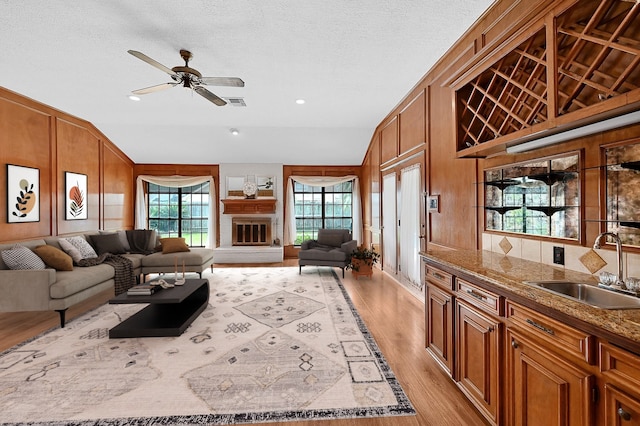 living room featuring ceiling fan, sink, light hardwood / wood-style flooring, wood walls, and vaulted ceiling