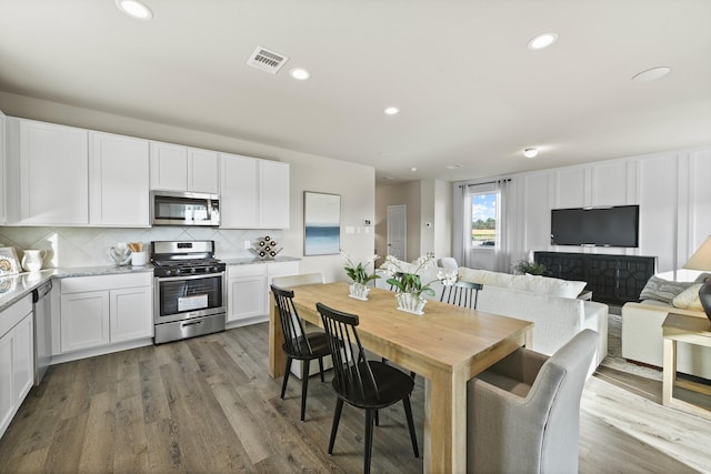 kitchen featuring white cabinetry, dark wood-type flooring, stainless steel appliances, light stone counters, and decorative backsplash