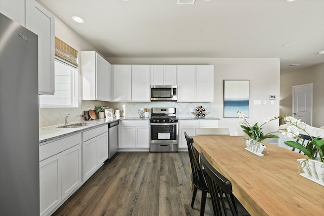 kitchen featuring dark hardwood / wood-style flooring, light stone counters, stainless steel appliances, sink, and white cabinetry