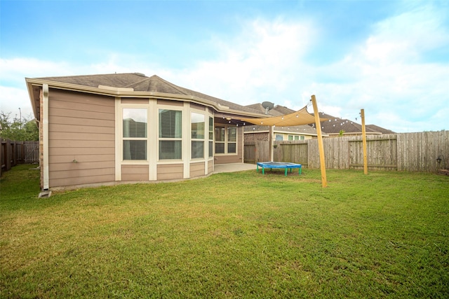 rear view of property featuring a lawn and a trampoline