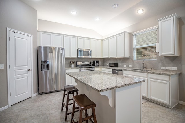 kitchen with sink, vaulted ceiling, a kitchen island, white cabinetry, and stainless steel appliances