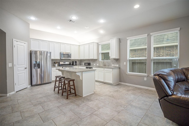 kitchen featuring stainless steel appliances, a kitchen island, white cabinetry, and lofted ceiling