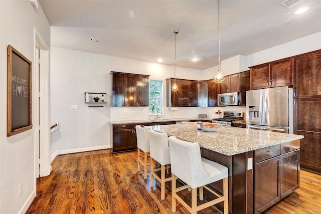 kitchen with light stone counters, dark hardwood / wood-style floors, decorative light fixtures, a kitchen island, and appliances with stainless steel finishes