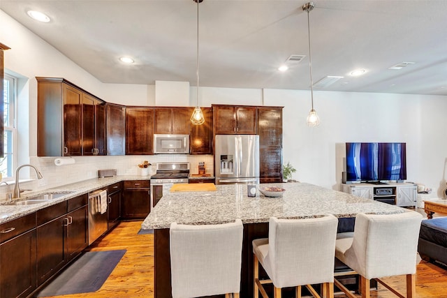 kitchen with light stone countertops, sink, stainless steel appliances, decorative light fixtures, and a kitchen island