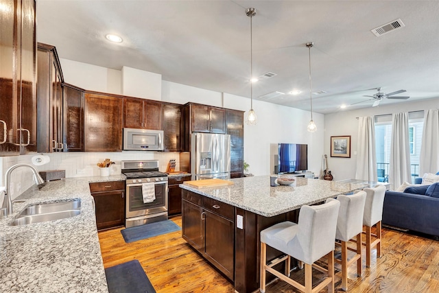 kitchen with sink, a center island, light stone counters, backsplash, and appliances with stainless steel finishes