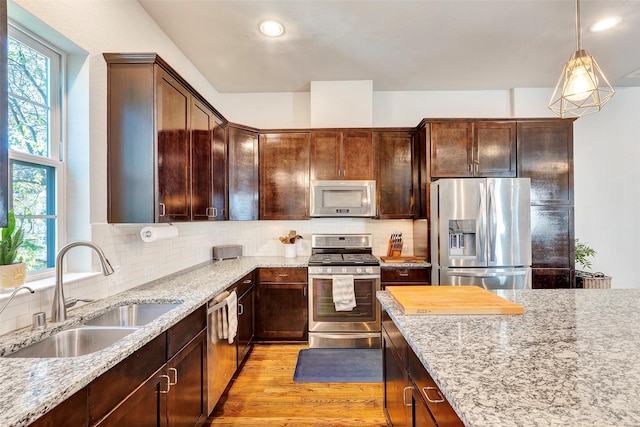 kitchen with pendant lighting, sink, decorative backsplash, light stone counters, and stainless steel appliances