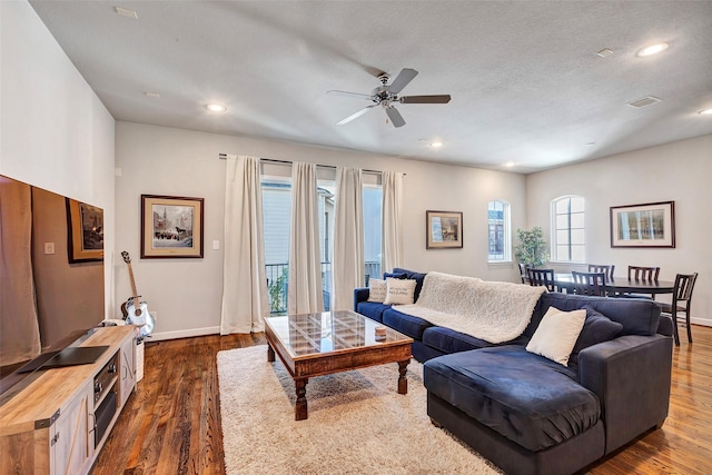 living room with a textured ceiling, ceiling fan, and dark wood-type flooring