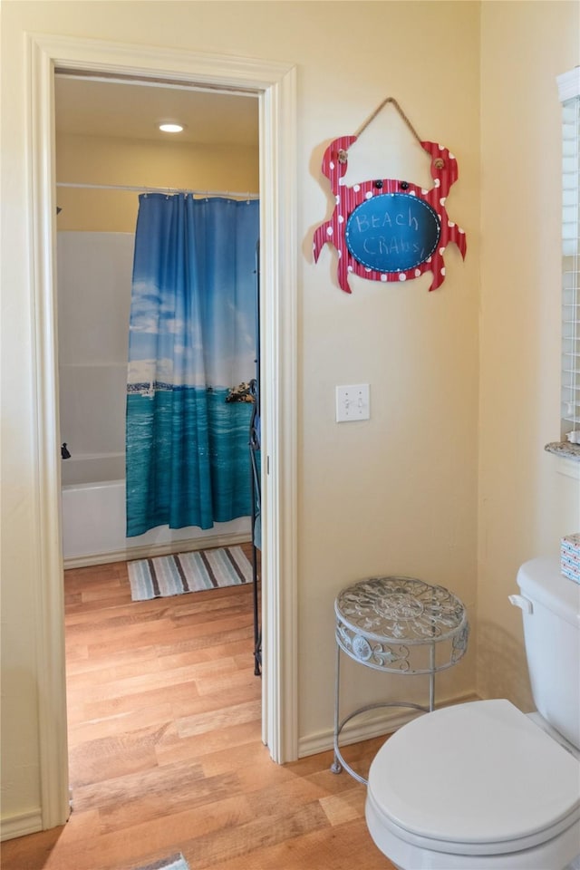 bathroom with hardwood / wood-style flooring, shower / bath combination with curtain, and toilet