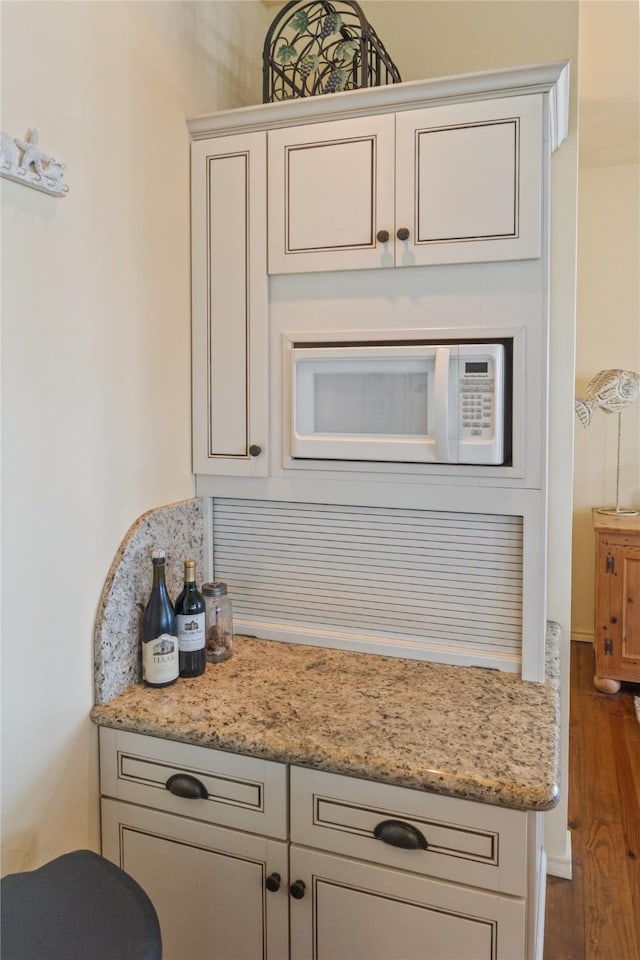 kitchen with white cabinetry, light stone countertops, wood-type flooring, and white microwave