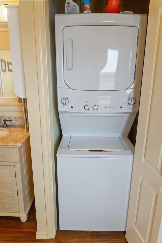 laundry room with stacked washer / dryer, dark hardwood / wood-style flooring, and sink