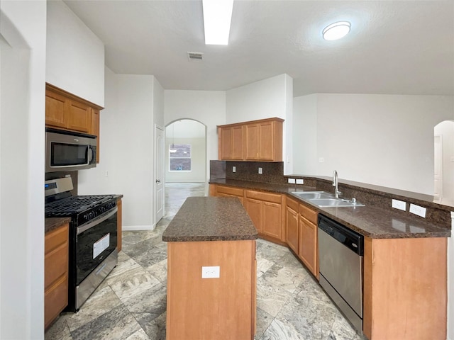 kitchen with kitchen peninsula, appliances with stainless steel finishes, a kitchen island, and sink