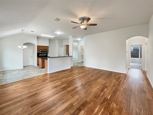 unfurnished living room with ceiling fan with notable chandelier, lofted ceiling, and light hardwood / wood-style flooring