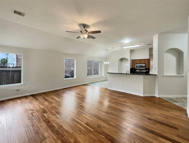 unfurnished living room with hardwood / wood-style flooring, ceiling fan with notable chandelier, and lofted ceiling