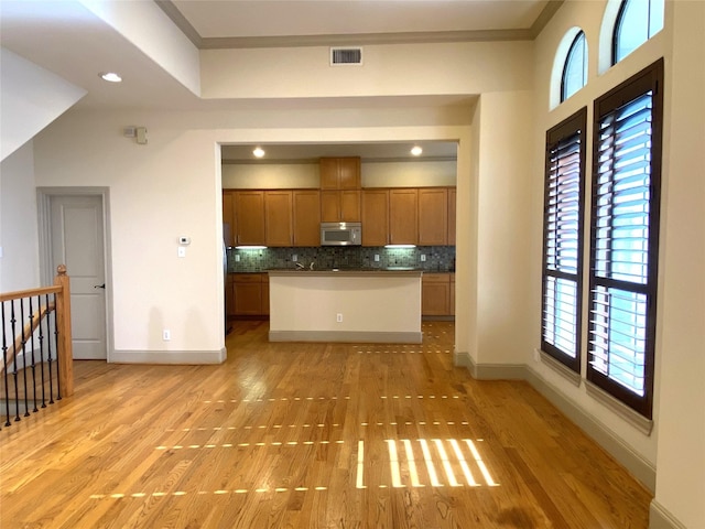 kitchen with tasteful backsplash, ornamental molding, and light wood-type flooring