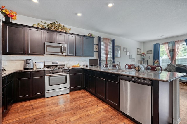 kitchen featuring sink, stainless steel appliances, light hardwood / wood-style flooring, kitchen peninsula, and a textured ceiling