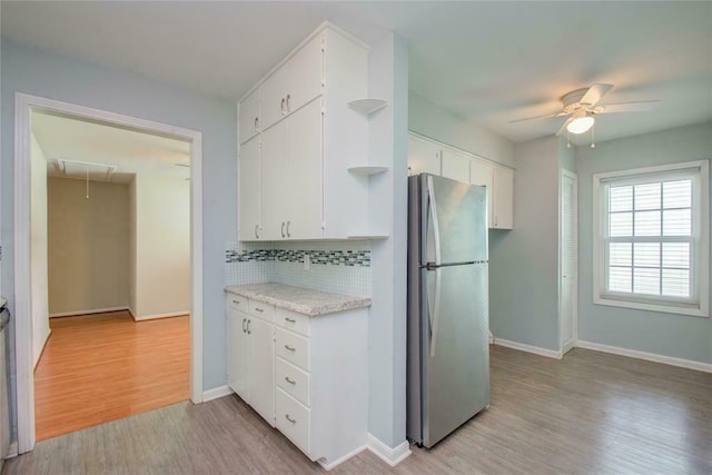 kitchen featuring white cabinets, decorative backsplash, ceiling fan, light wood-type flooring, and stainless steel refrigerator