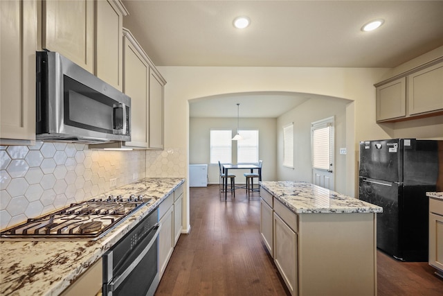 kitchen featuring a center island, hanging light fixtures, appliances with stainless steel finishes, cream cabinetry, and dark hardwood / wood-style flooring