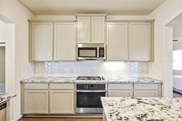 kitchen featuring cream cabinetry, appliances with stainless steel finishes, decorative backsplash, and light stone counters