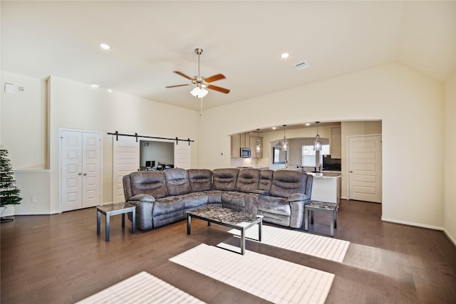 living room featuring ceiling fan, a barn door, dark wood-type flooring, and vaulted ceiling