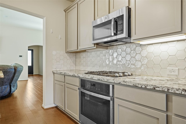 kitchen with backsplash, light stone countertops, light hardwood / wood-style floors, and appliances with stainless steel finishes