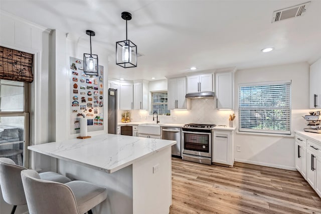 kitchen with white cabinetry, sink, stainless steel appliances, and decorative light fixtures