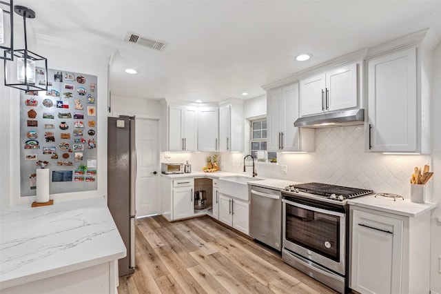 kitchen with light stone countertops, light hardwood / wood-style floors, decorative light fixtures, white cabinets, and appliances with stainless steel finishes