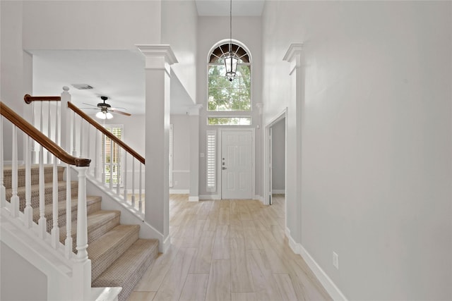 entryway featuring ceiling fan, light hardwood / wood-style floors, decorative columns, and a towering ceiling