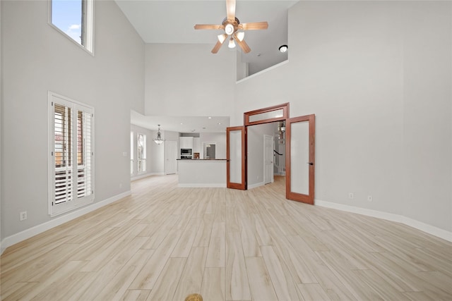 unfurnished living room featuring french doors, a towering ceiling, ceiling fan with notable chandelier, and light hardwood / wood-style floors