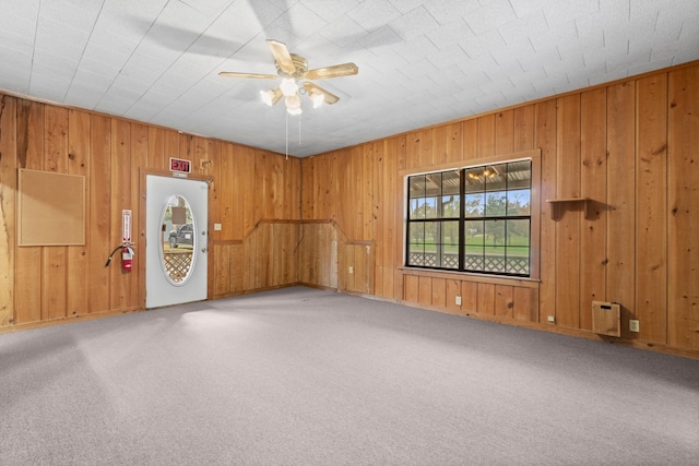 carpeted empty room with ceiling fan and wooden walls