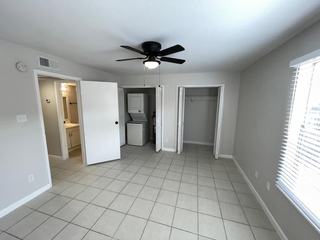 unfurnished bedroom with light tile patterned floors, ensuite bath, stacked washer / dryer, and ceiling fan