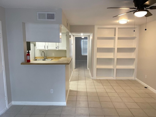 kitchen featuring sink, kitchen peninsula, ceiling fan, light tile patterned floors, and white cabinetry