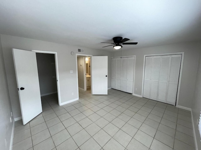 unfurnished bedroom featuring ceiling fan, light tile patterned floors, ensuite bathroom, and multiple closets