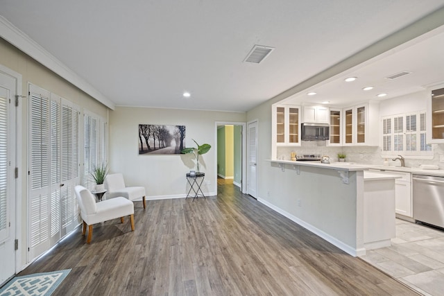 kitchen with a kitchen breakfast bar, appliances with stainless steel finishes, hardwood / wood-style flooring, white cabinetry, and decorative backsplash