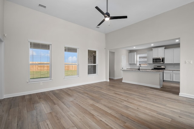 unfurnished living room featuring sink, a high ceiling, plenty of natural light, and light wood-type flooring