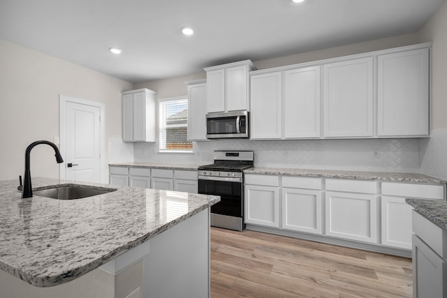 kitchen with white cabinets, a center island with sink, sink, appliances with stainless steel finishes, and light stone counters