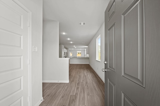 corridor with light wood finished floors, baseboards, and visible vents