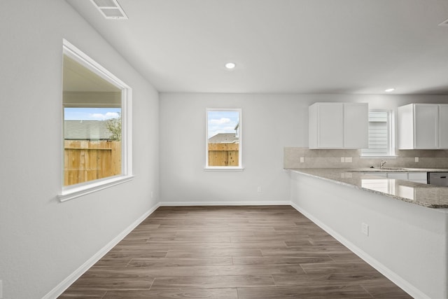 kitchen with light stone counters, dark wood-style flooring, tasteful backsplash, white cabinets, and baseboards