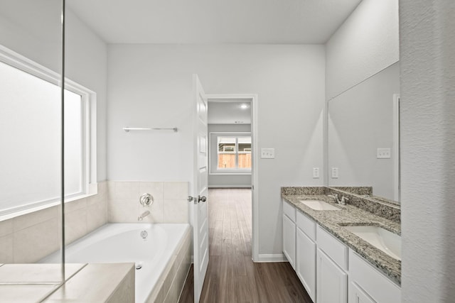 bathroom with double vanity, a garden tub, a sink, and wood finished floors