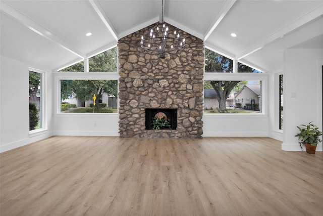 unfurnished living room with a chandelier, lofted ceiling with beams, light hardwood / wood-style flooring, and a stone fireplace