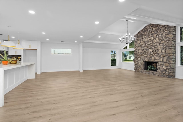 unfurnished living room featuring lofted ceiling with beams, light hardwood / wood-style flooring, a stone fireplace, and a notable chandelier